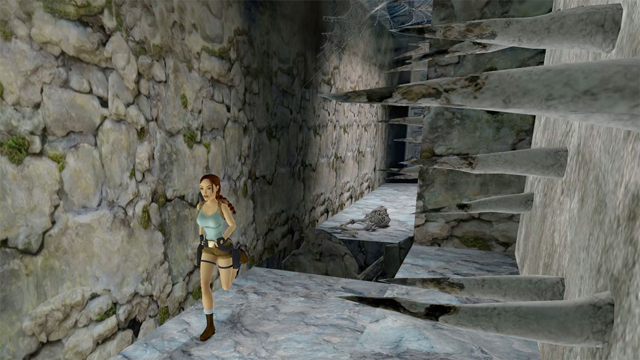 Lara Croft rent door een stenen gang langs scherpe houten spiesen die uit de muur steken.
