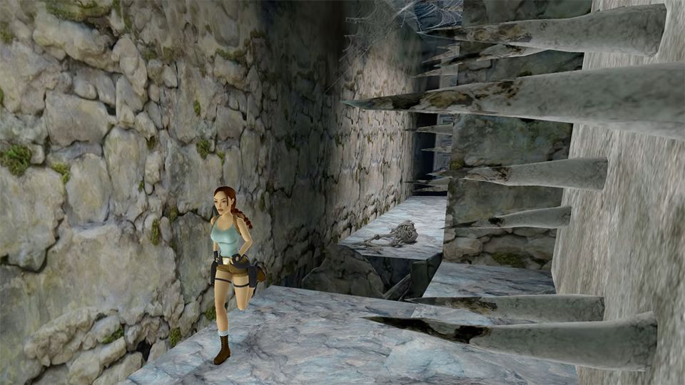 Lara Croft rent door een stenen gang langs scherpe houten spiesen die uit de muur steken.