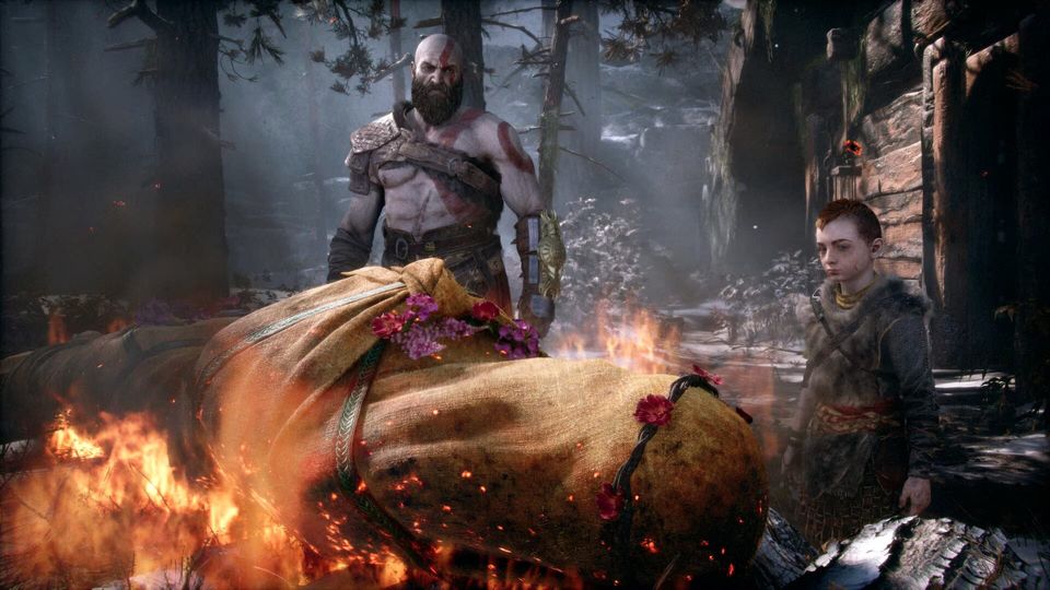 Kratos en Atreus staan bij een brandende brandstapel in het bos.